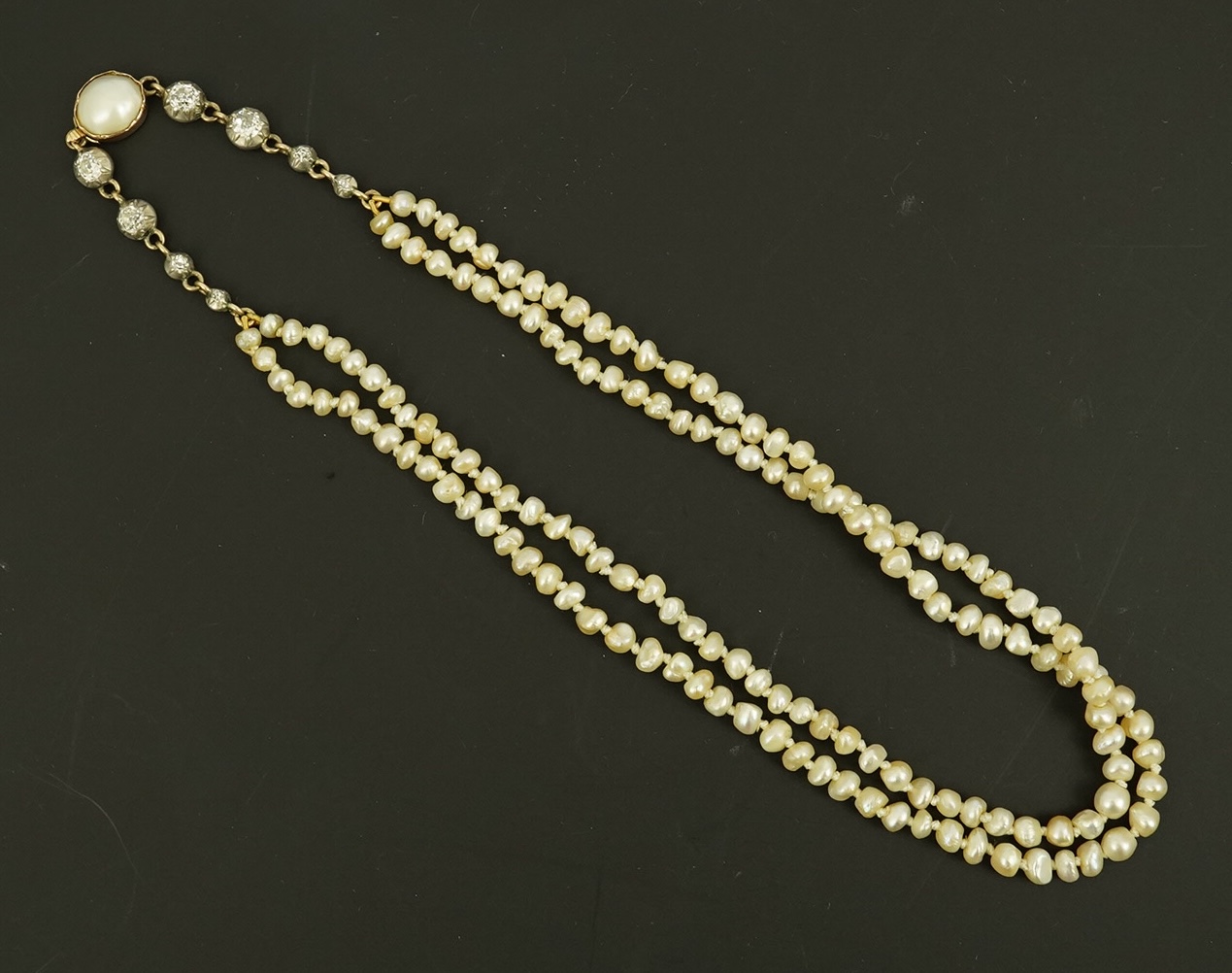 An antique twin strand baroque pearl necklace, with pearl set gold clasp bordered with single chain set with four graduated old mine cut diamonds